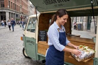 Femme entrepreneur gérant un triporteur food truck dans une rue piétonne urbaine avec menu ardoise et comptoir bois