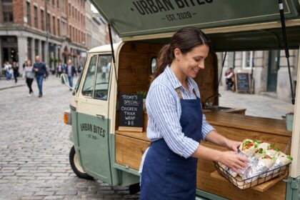 Femme entrepreneur gérant un triporteur food truck dans une rue piétonne urbaine avec menu ardoise et comptoir bois