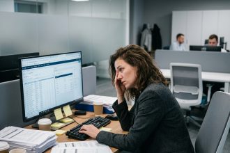 Commerciale B2B débordée à son bureau avec des données de prospection affichées sur écran, illustrant la saturation des équipes internes