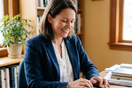 Femme souriante tapant un avis positif sur son smartphone dans un bureau à domicile, illustrant le bouche-à-oreille numérique